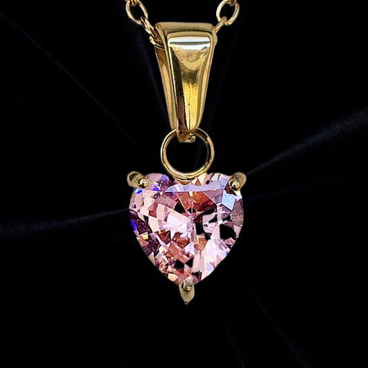 Guld halsband med rosa hjärt formad sten på svart sammetstyg i bakgrunden