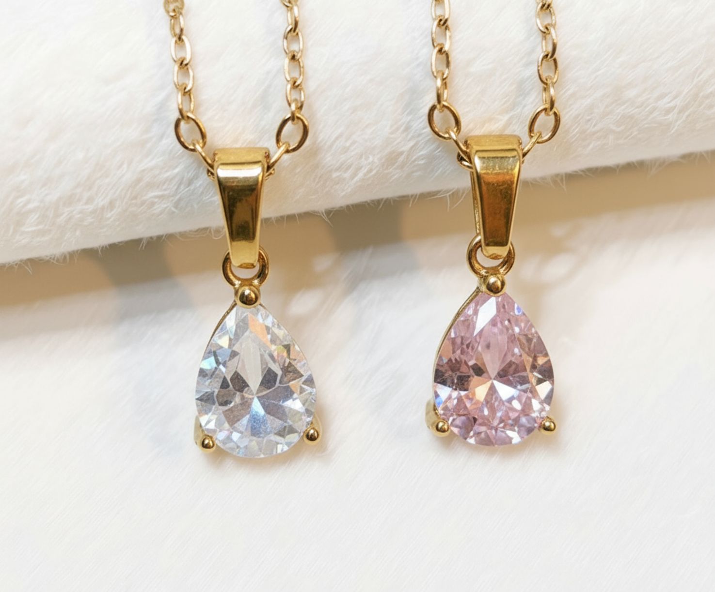Två halsband i guld med droppformad kristallsten - på vit tyg bakgrund